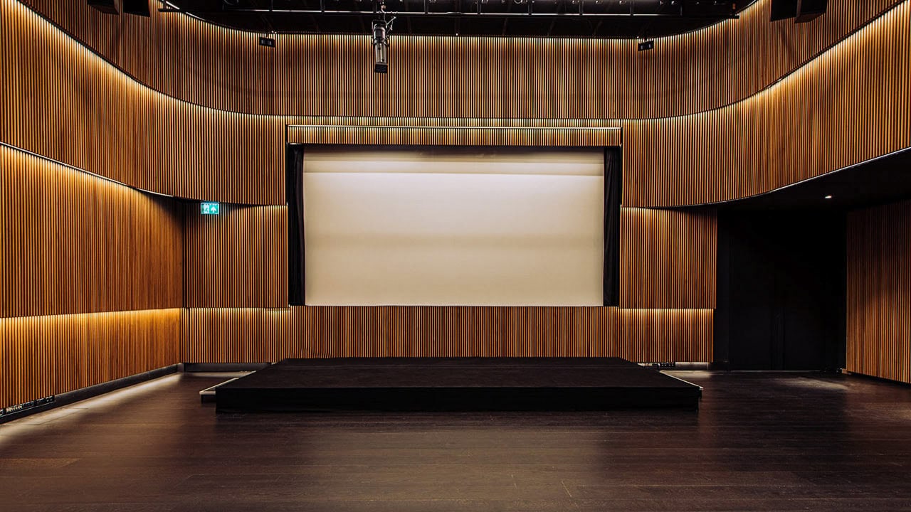 Museum auditorium with acoustic timber slat walls, stage and projection screen.
