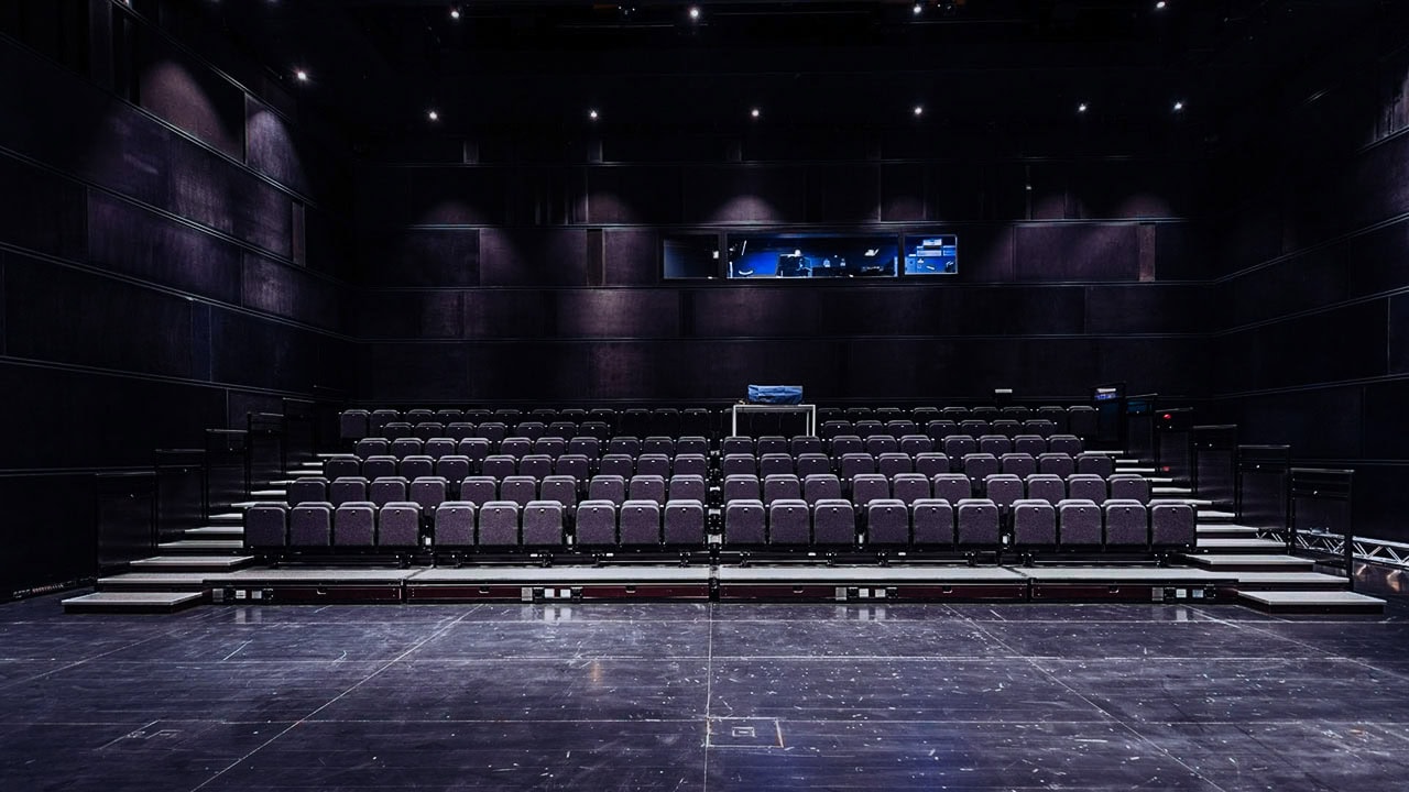 Auditorio del museo visto desde el escenario, con butacas escalonadas y superficies acústicas oscuras bajo luz teatral.