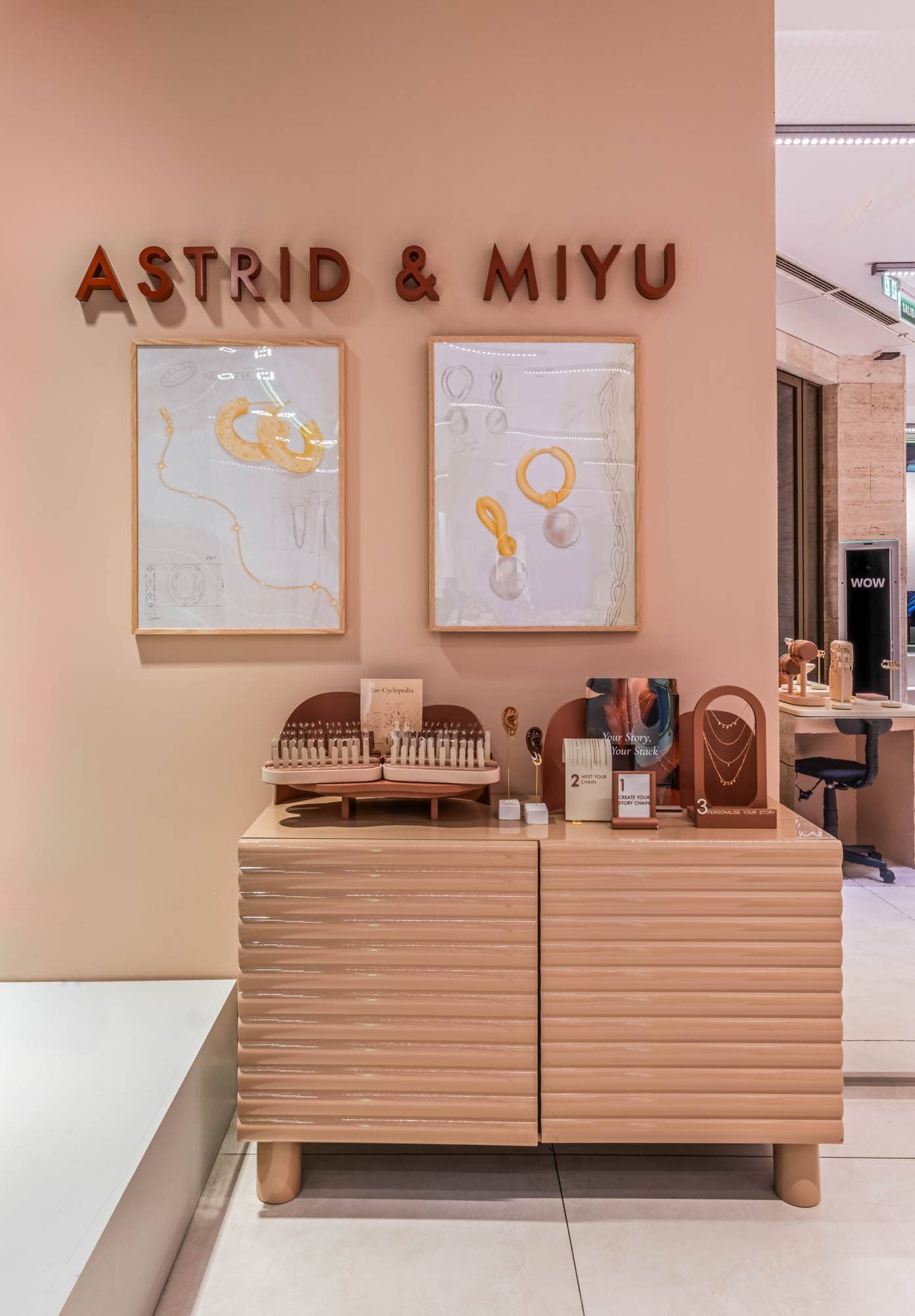 Muro de marca de Astrid and Miyu con obra enmarcada sobre un expositor de joyería de madera.