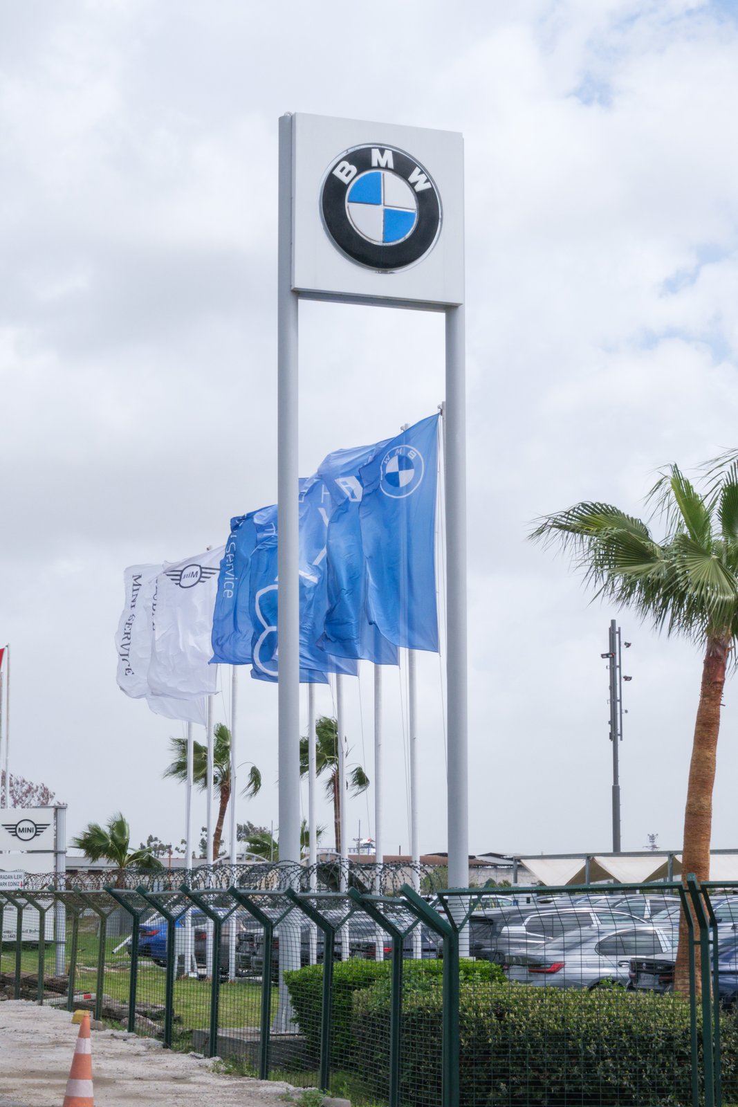 Tótem BMW en la entrada de un concesionario con la línea de banderas detrás.