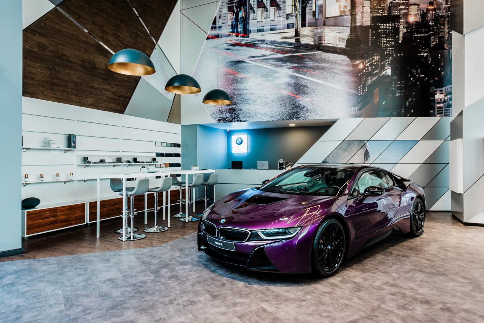BMW i8 expuesto en la zona lounge de un concesionario con luminarias colgantes y asientos para clientes.