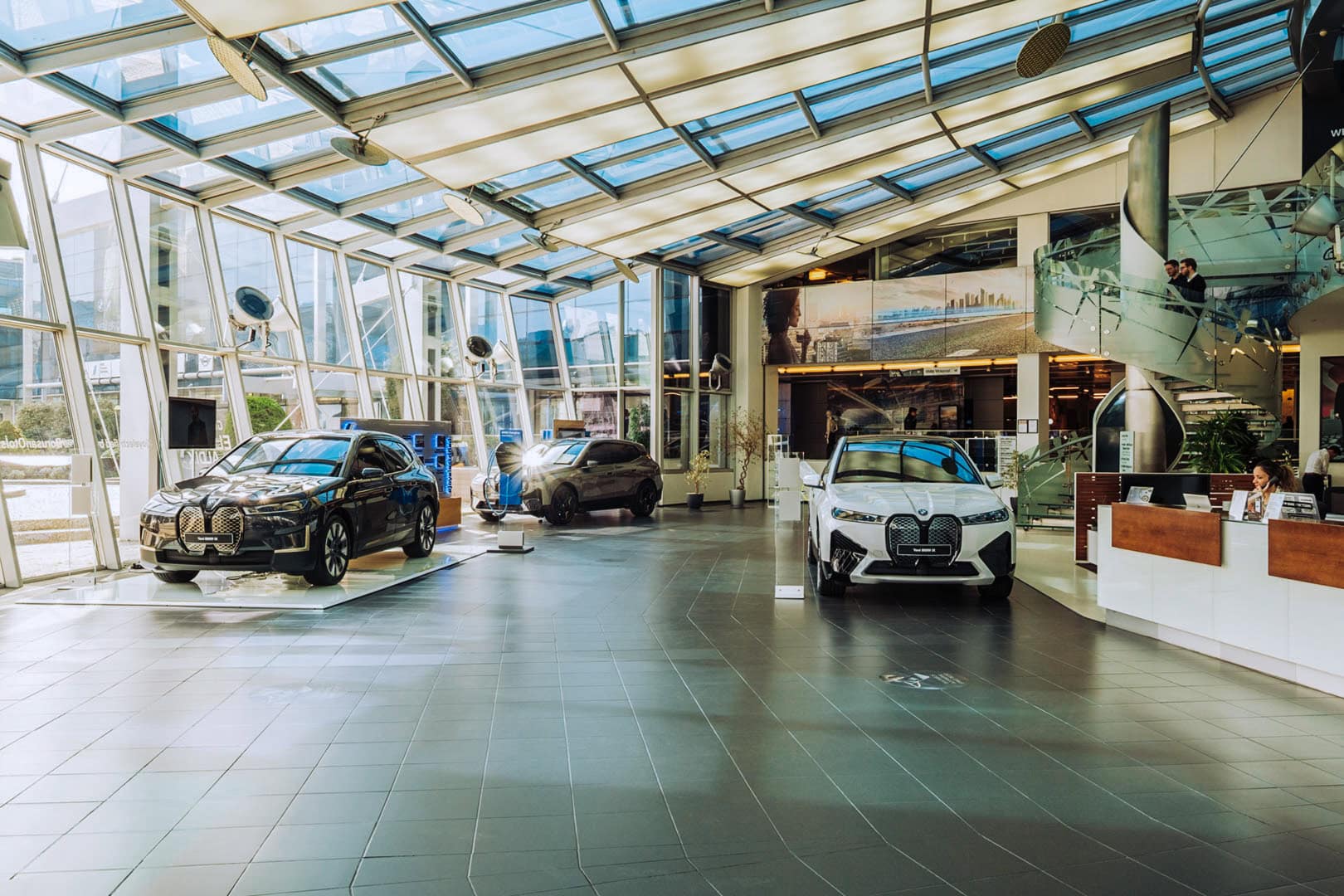 Sala de exposición BMW con vehículos dispuestos bajo una cubierta acristalada con luz natural.