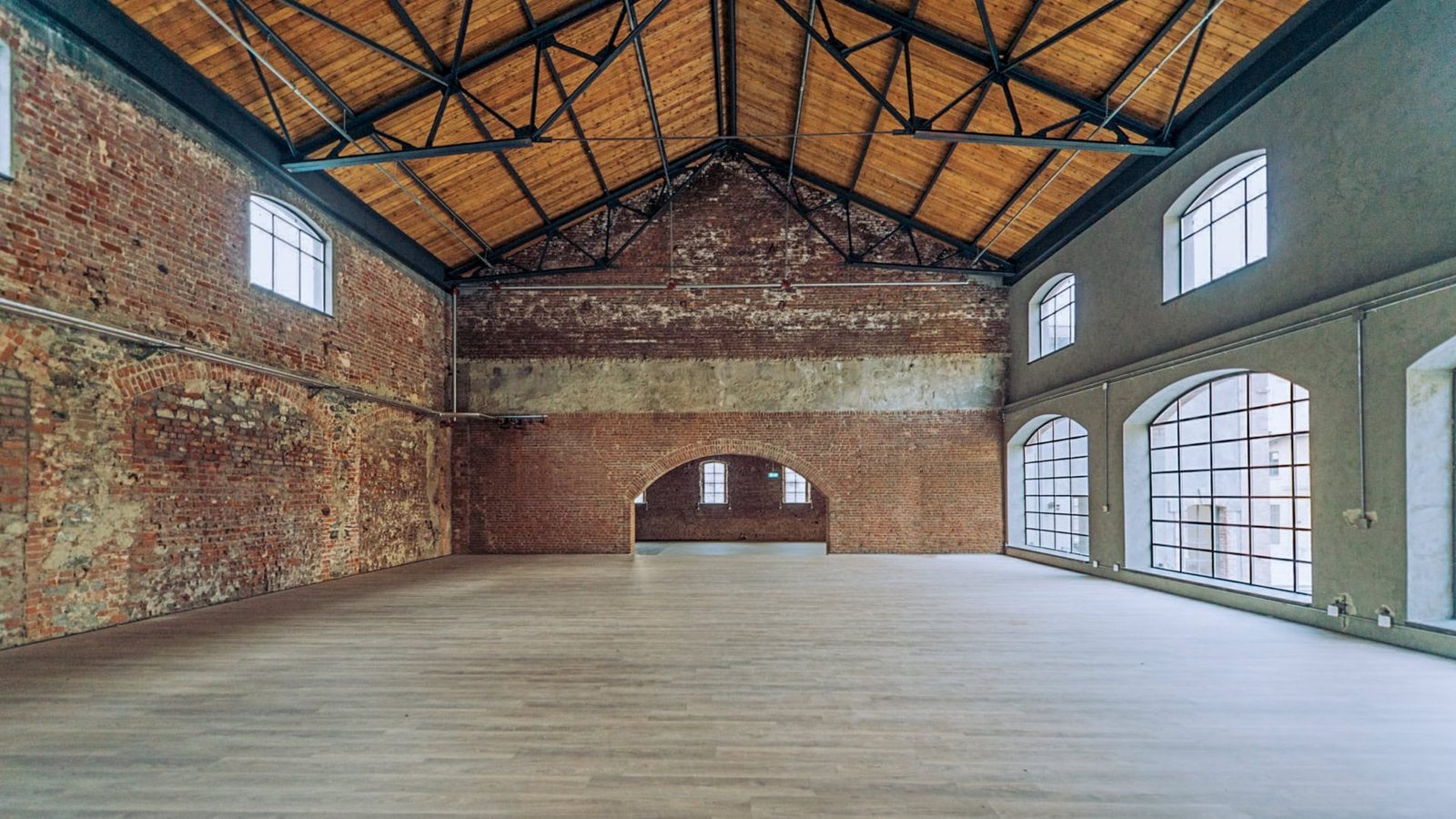Restored gallery space with exposed brick walls and original timber roof trusses above a polished floor.