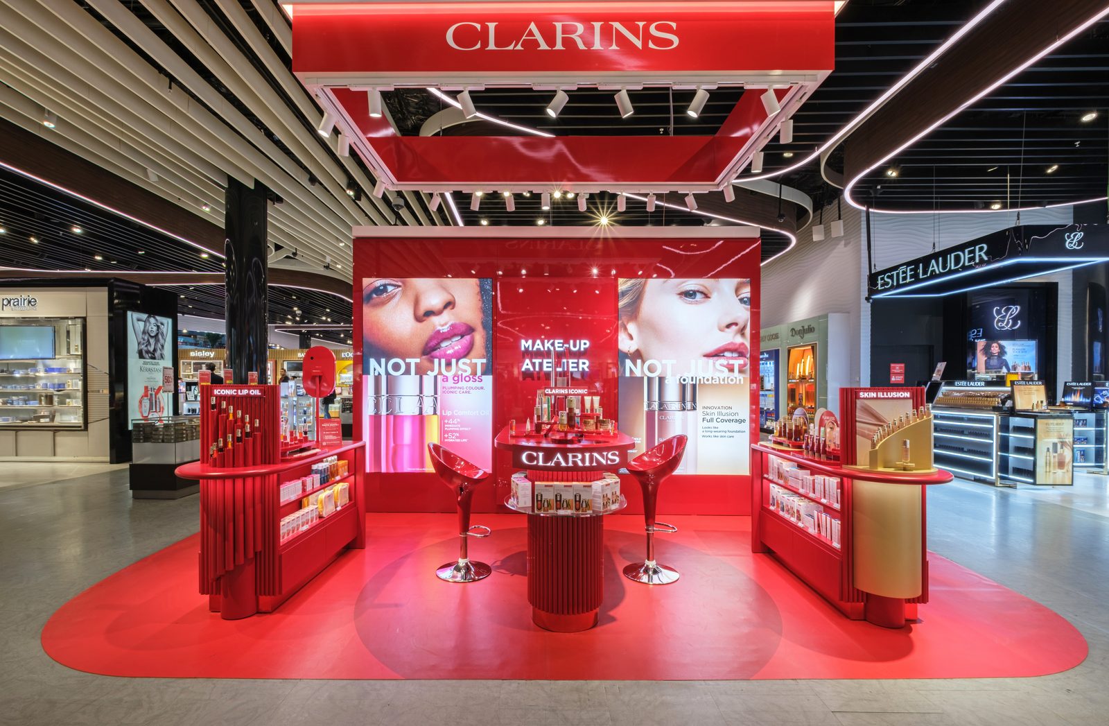 Red Clarins Make-Up Atelier booth with its suspended logo frame in an airport duty free store.