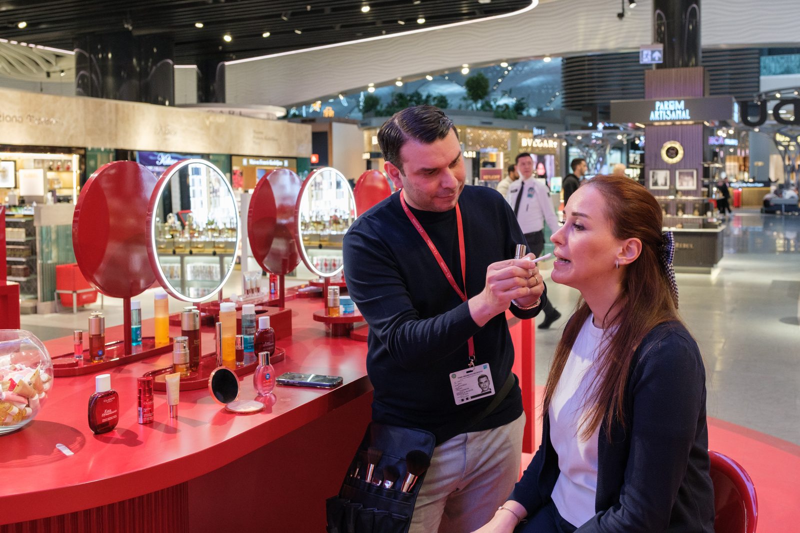 Makeup artist working with a guest at the Clarins Make-Up Atelier inside an airport duty free store.