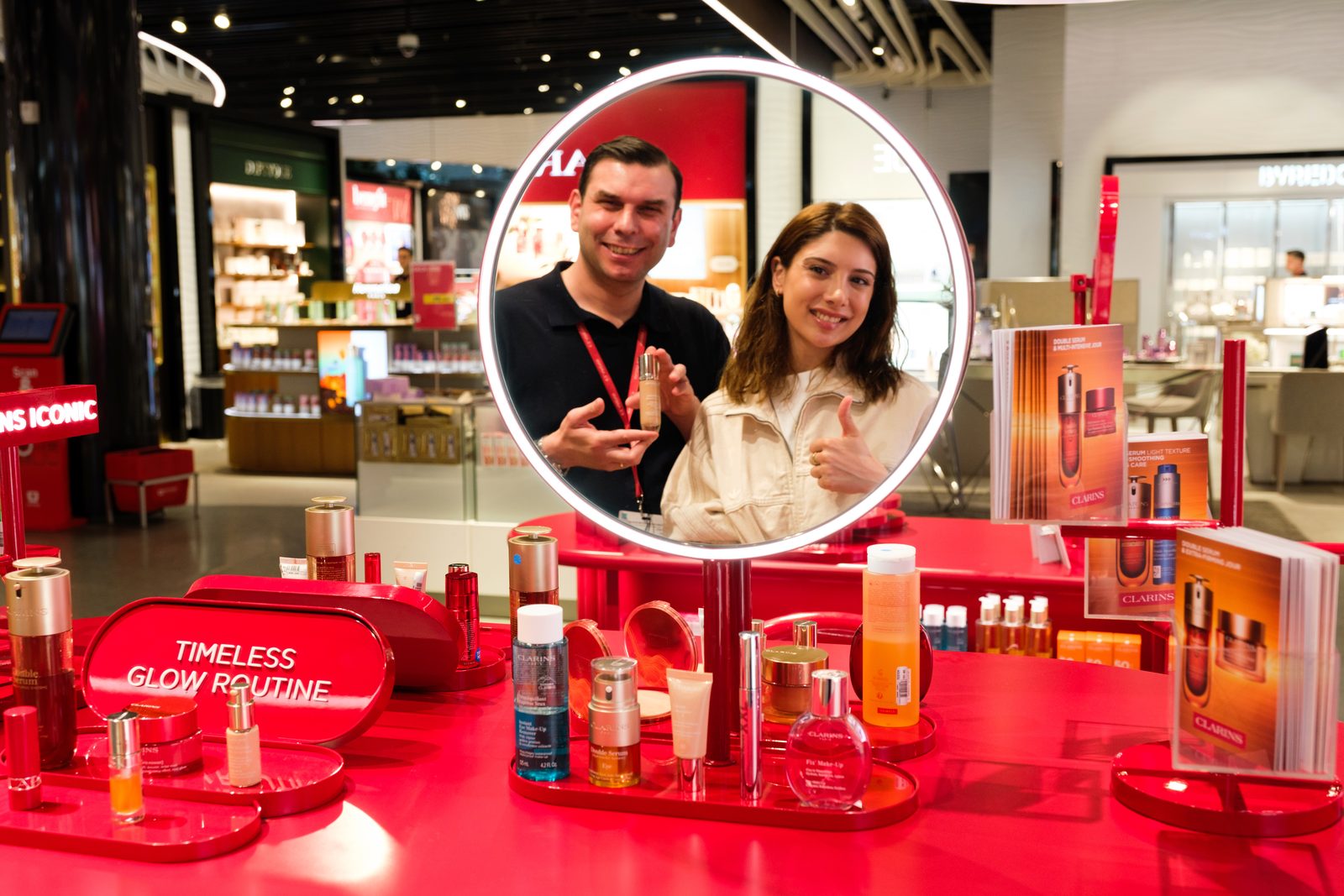 Makeup artist and guest reflected in the illuminated mirror of the Clarins Make-Up Atelier during an activation.
