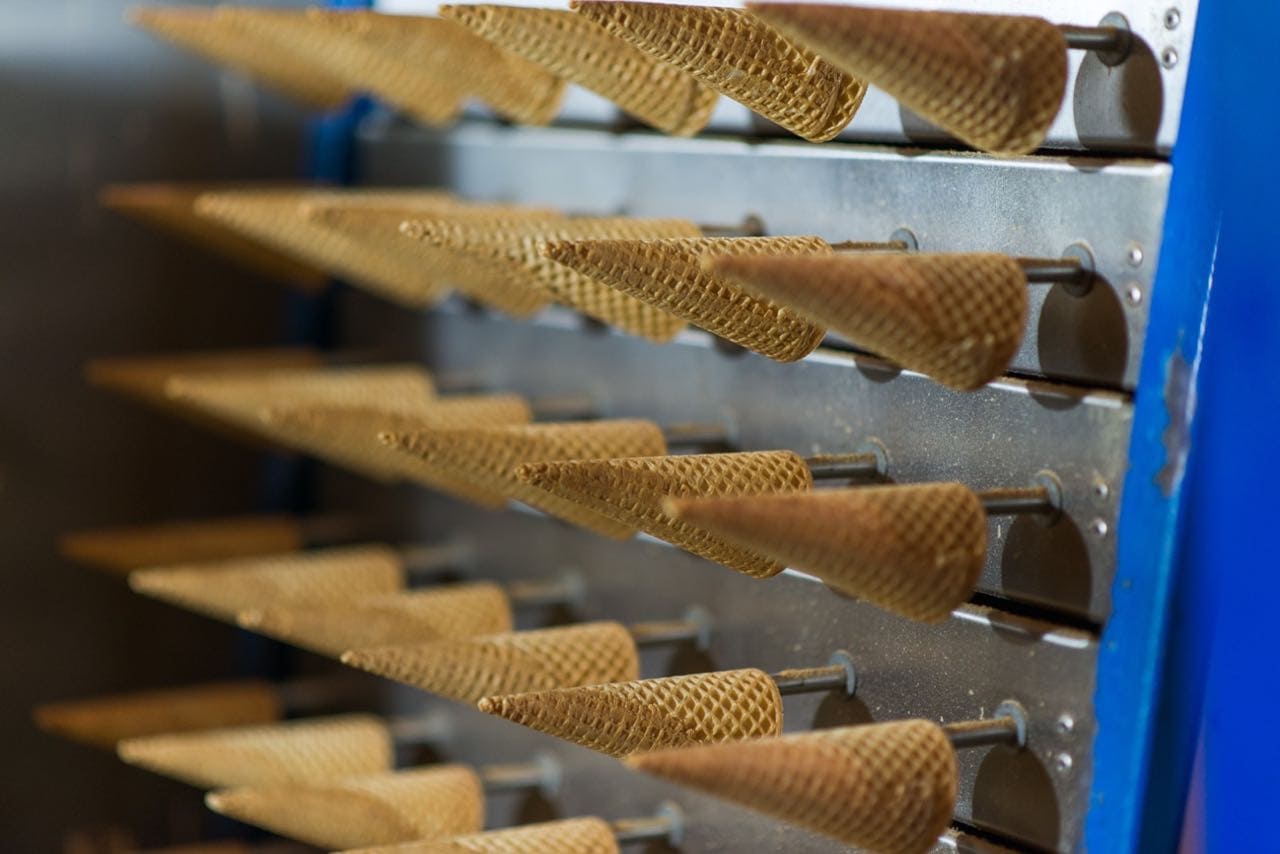 Rows of waffle cones held in stainless steel racks on an ice cream production line.