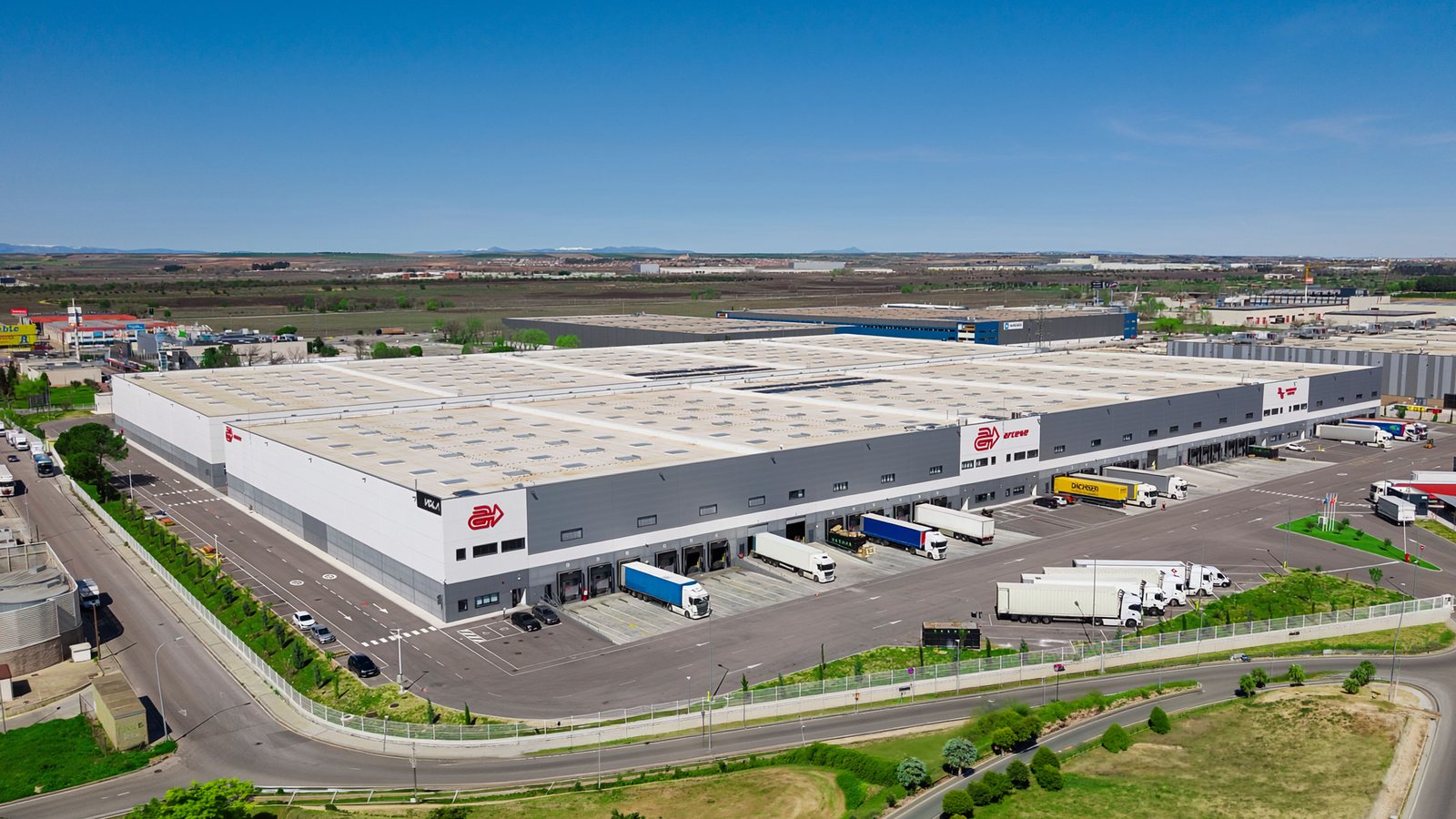 Vista aérea de un gran complejo logístico en el corredor del Henares, con línea de muelles, patio de camiones y acceso a la autovía.