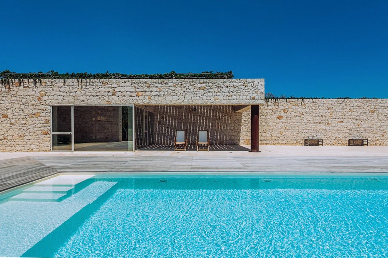 Villa moderna de piedra con piscina rectangular y terraza cubierta, fotografía de arquitectura de lujo en Sicilia, Italia.