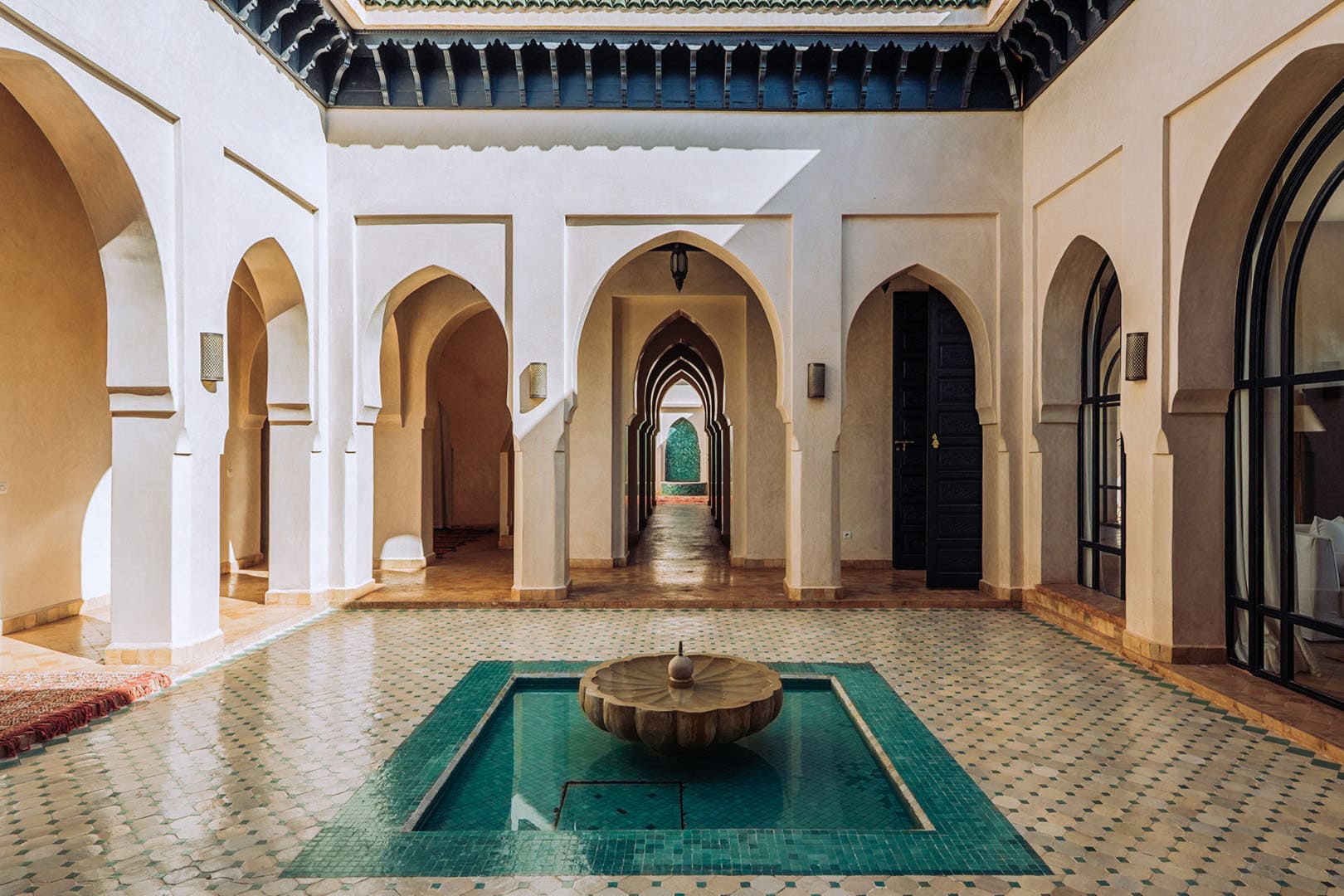 Patio interior elegante de estilo marroquí con arcos, suelo de azulejo de trazado complejo y una fuente central, para fotografía de arquitectura y hostelería.