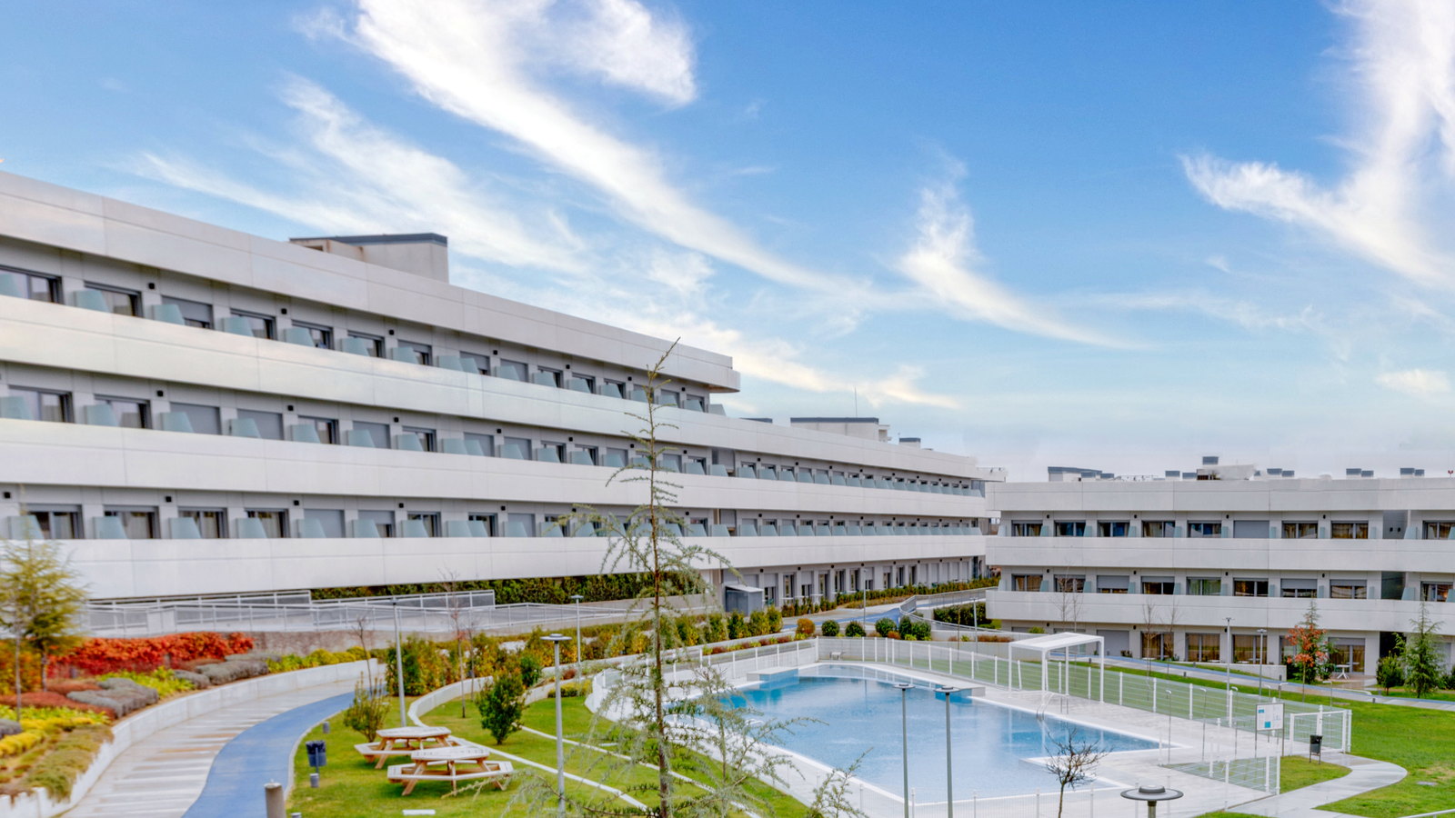 Curved facades of a student residence in Madrid around its landscaped courtyard and pool.