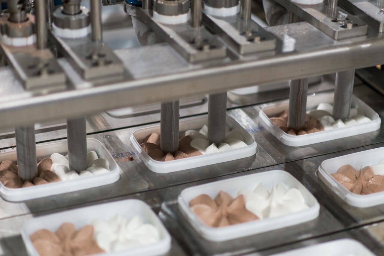 Ice cream tubs moving along an automated filling line inside a food manufacturing facility.