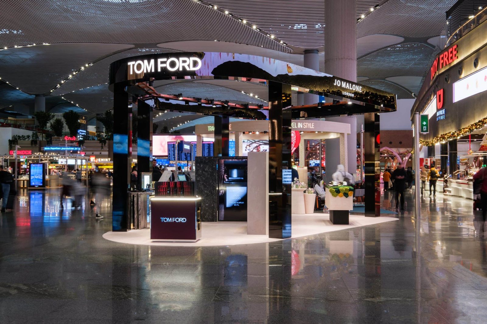 Espacio comercial de Tom Ford Beauty en la terminal de un aeropuerto internacional, con expositores de producto iluminados y flujo de pasajeros.