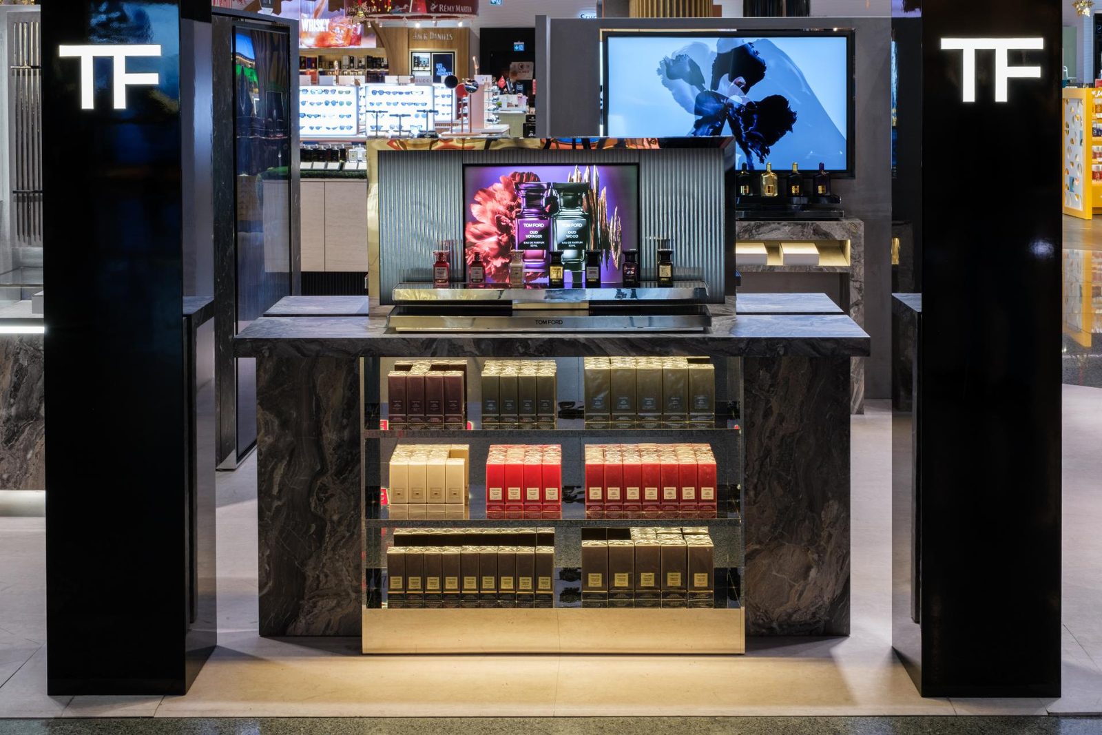 Tom Ford fragrance range on a backlit shelf display inside an airport duty free unit.
