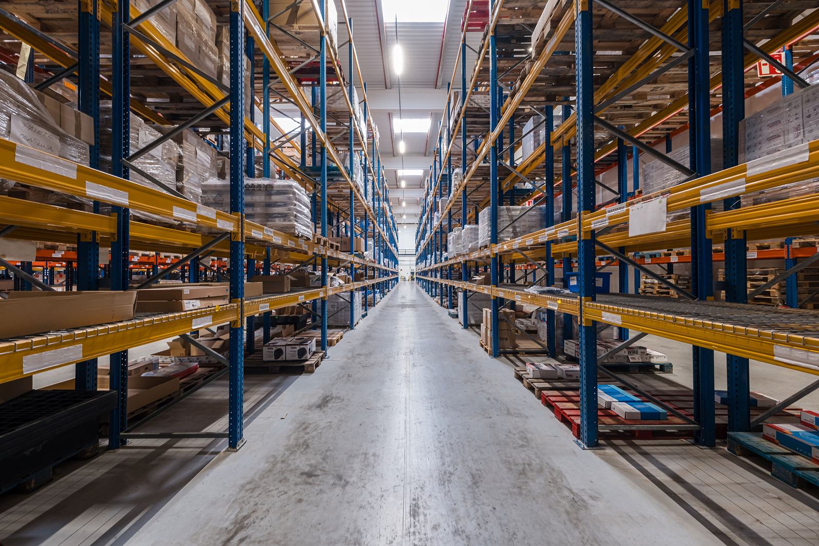 Warehouse racking aisle in one point perspective, loaded pallet racks receding to a bright vanishing point.