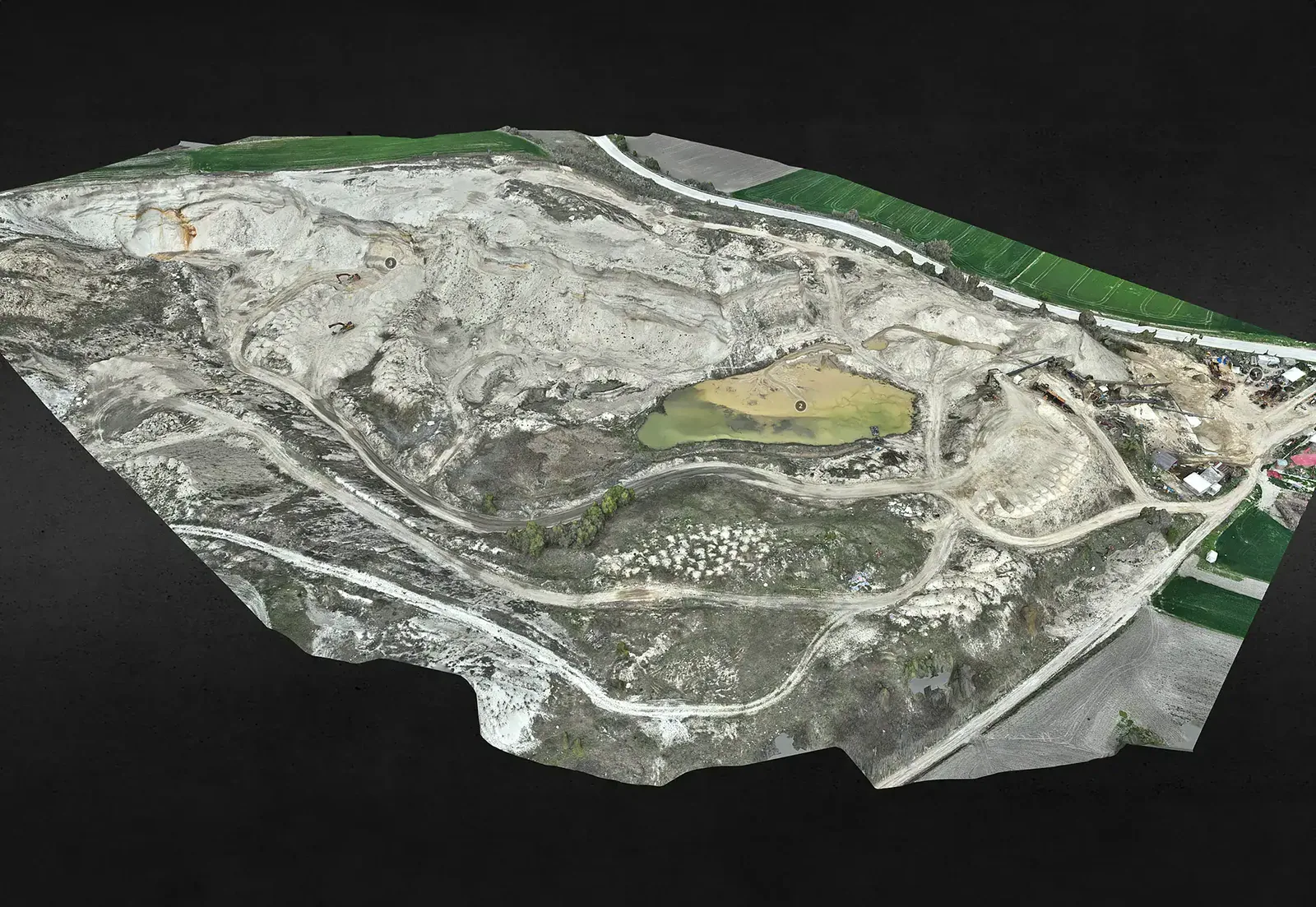 Aerial photogrammetry mesh of a large excavated earthworks and quarry site, showing haul roads, cut terraces and the green field boundary at the edge of the survey area.