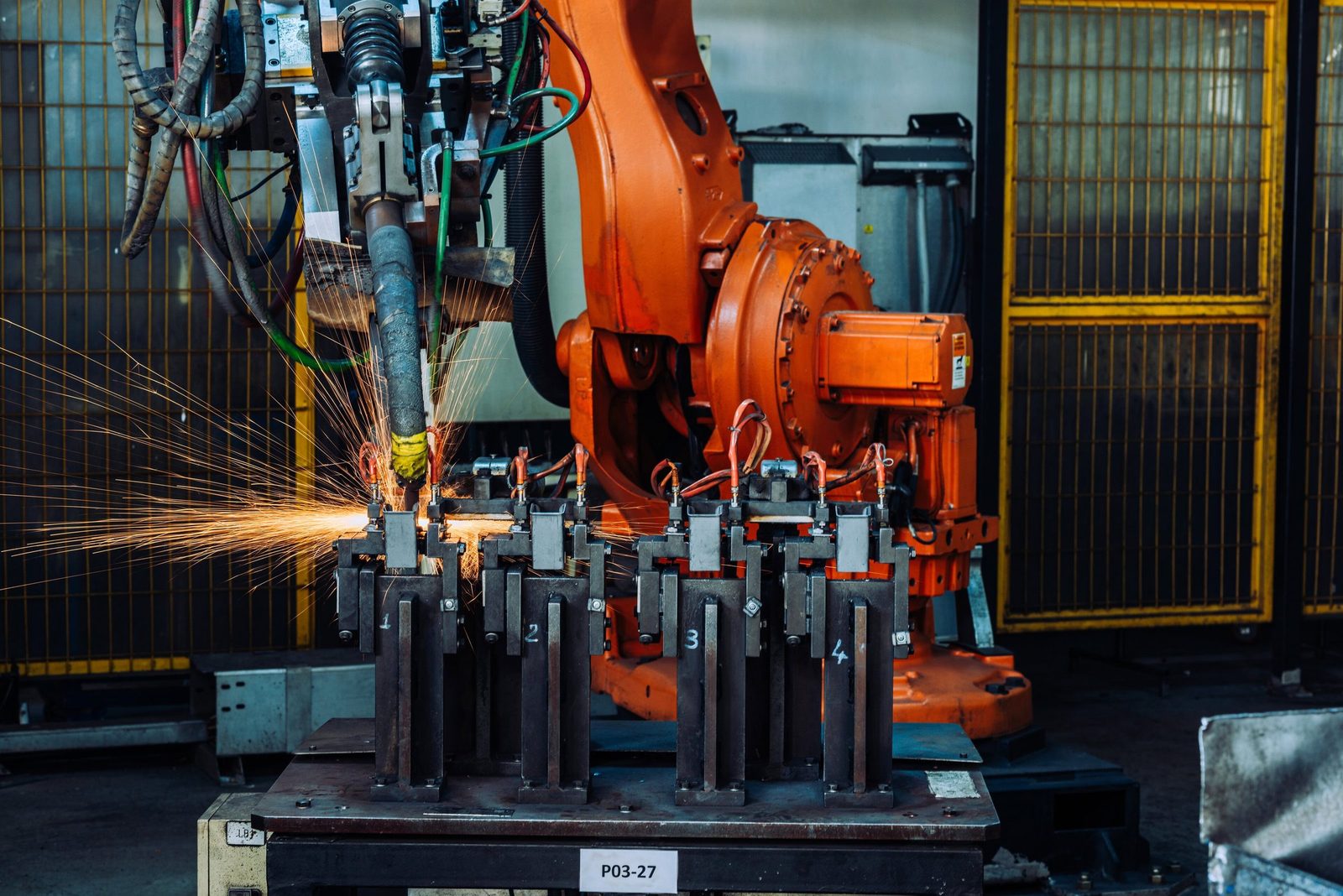 Robotic industrial machinery welding process with sparks flying in a factory setting.