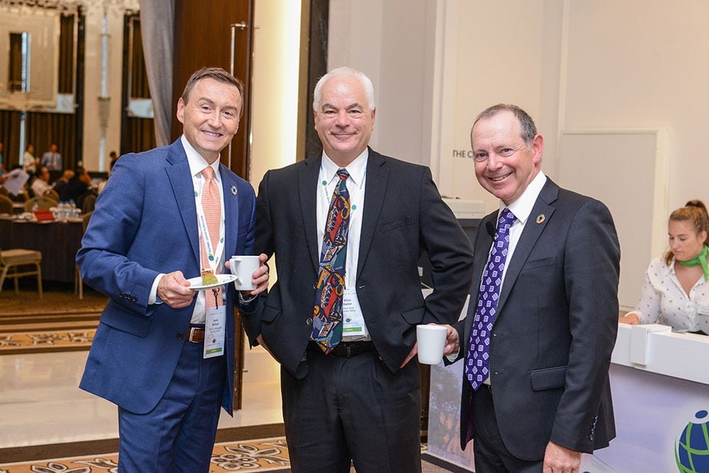 Three delegates in suits talking over coffee during a conference break.