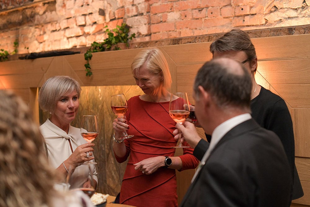 Guests raising glasses of wine at an evening networking reception against an exposed brick wall.