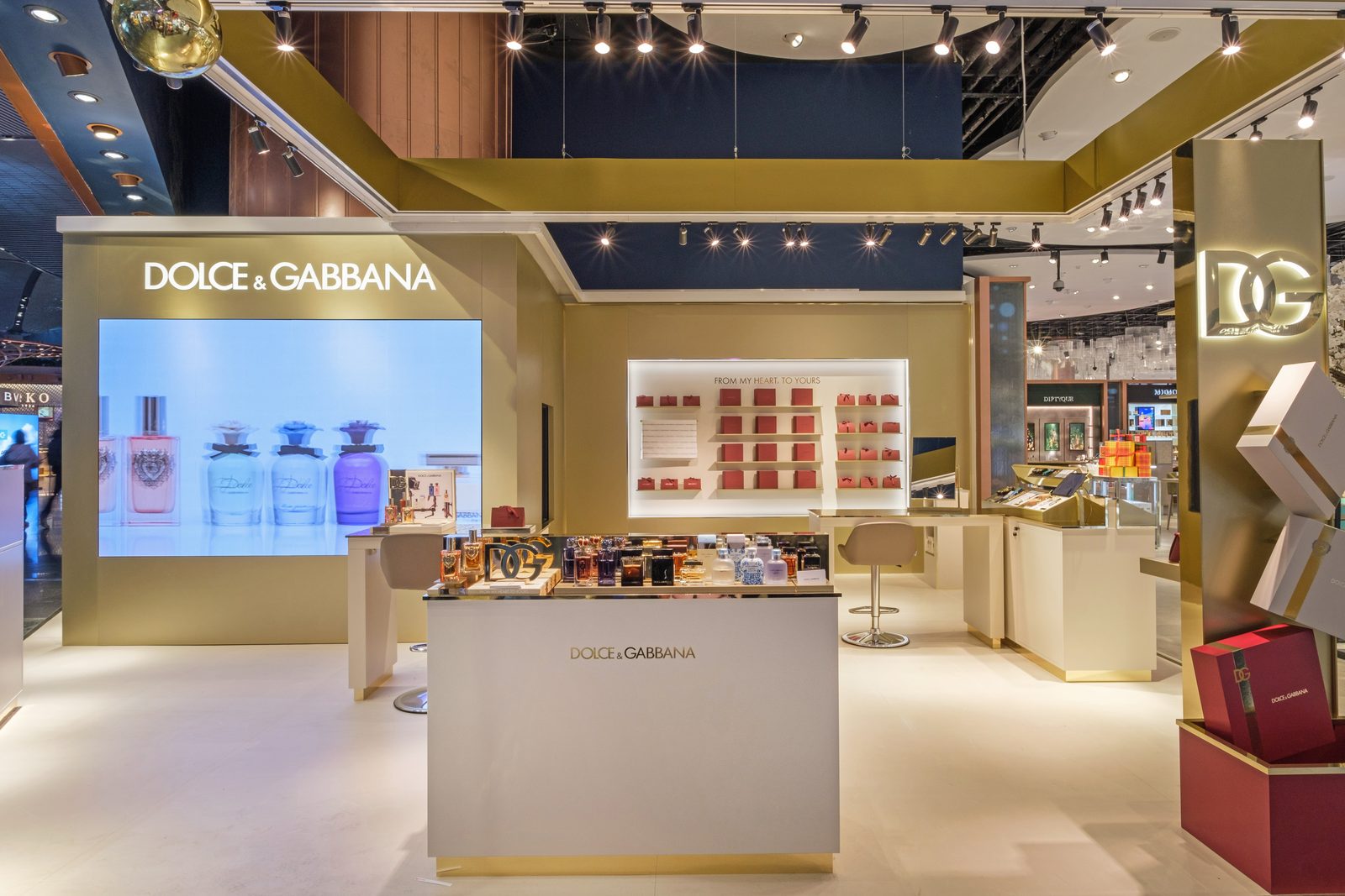 Dolce & Gabbana beauty boutique with gift wall, video screen and central counter in a duty free store.