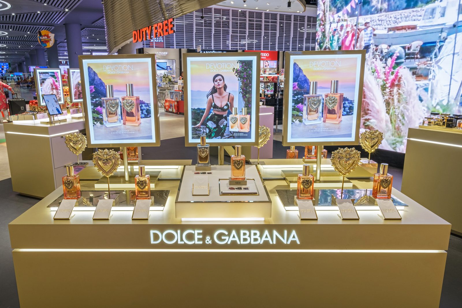Dolce & Gabbana fragrance counter with three lit campaign frames in a duty free store.