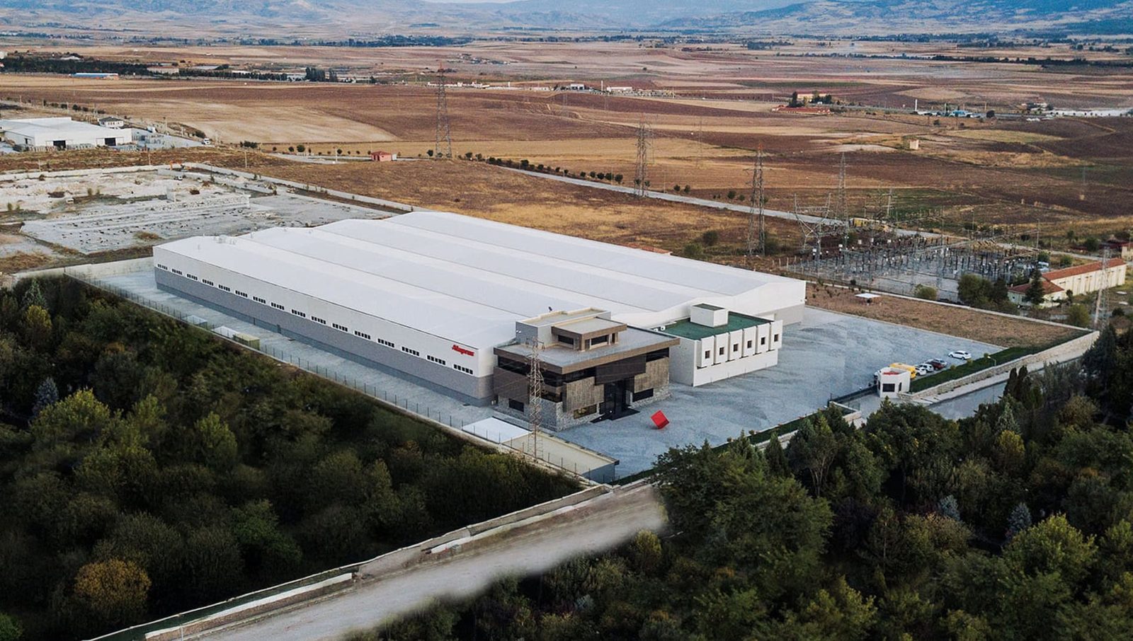 Aerial view of a modern production facility with a white roof, set among open fields and trees, Turkey.
