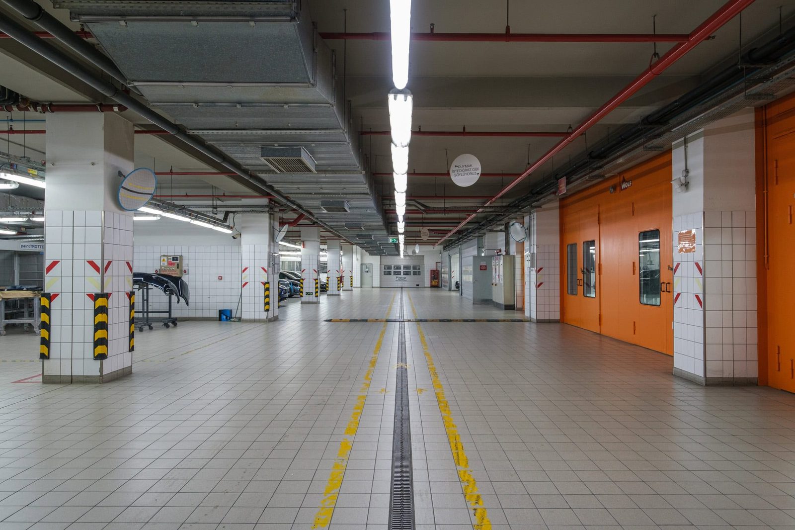 Empty service bay with white tiled walls, orange doors and exposed ceiling services at an automotive dealership, Istanbul.