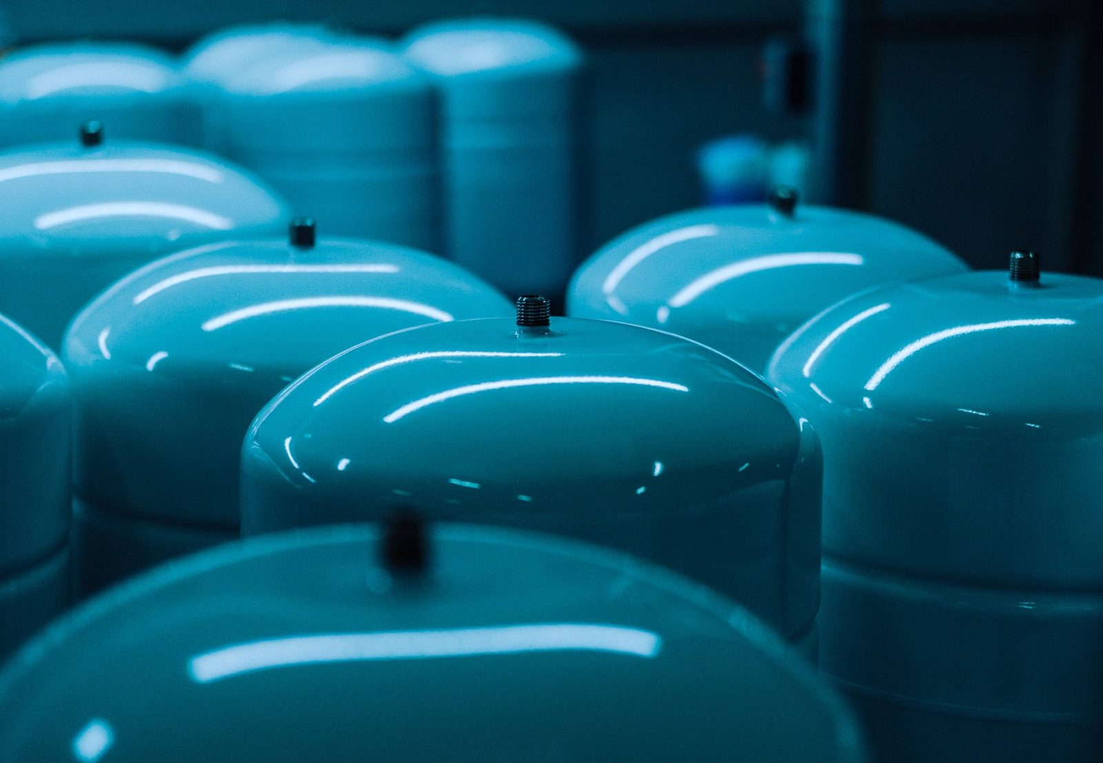 Blue industrial tanks with reflective surfaces in a manufacturing facility, illuminated by overhead lighting, showcasing industrial and commercial photography of manufacturing environments.