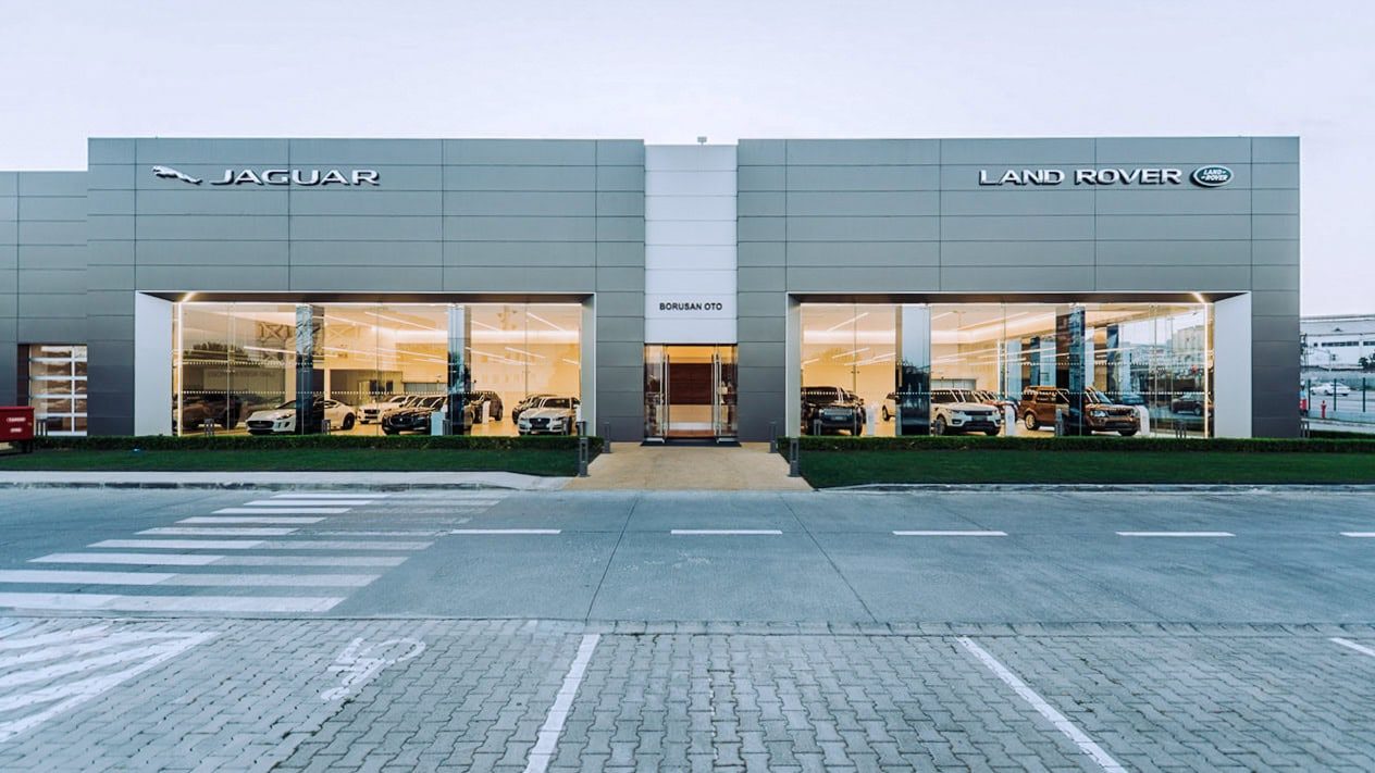 Concesionario insignia de Jaguar y Land Rover al anochecer, largo frente acristalado iluminado desde el interior.