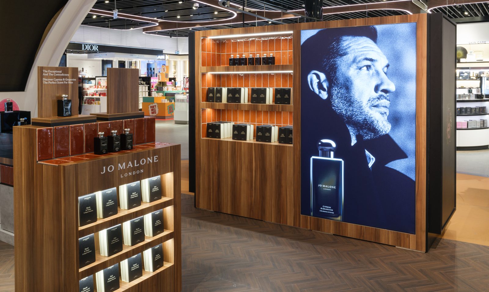 Jo Malone London fragrance wall in walnut with a lit campaign panel in a duty free store.