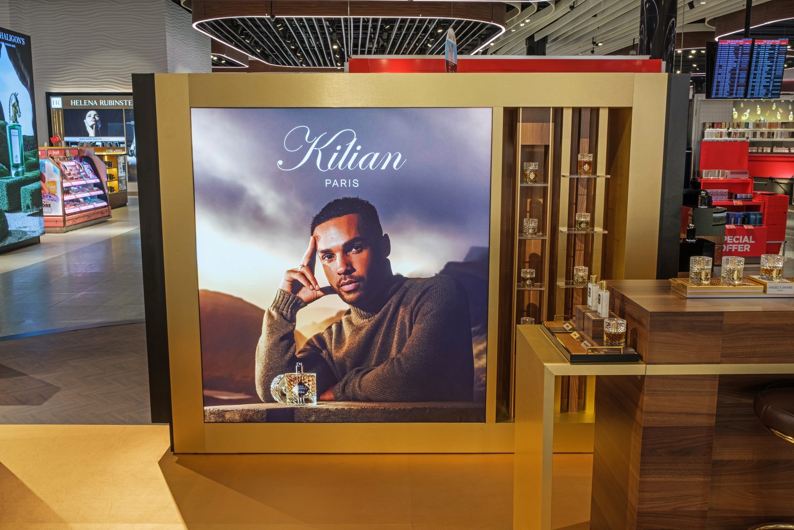 Kilian Paris fragrance bar with walnut counter, gold frame and campaign lightbox in a duty free store.