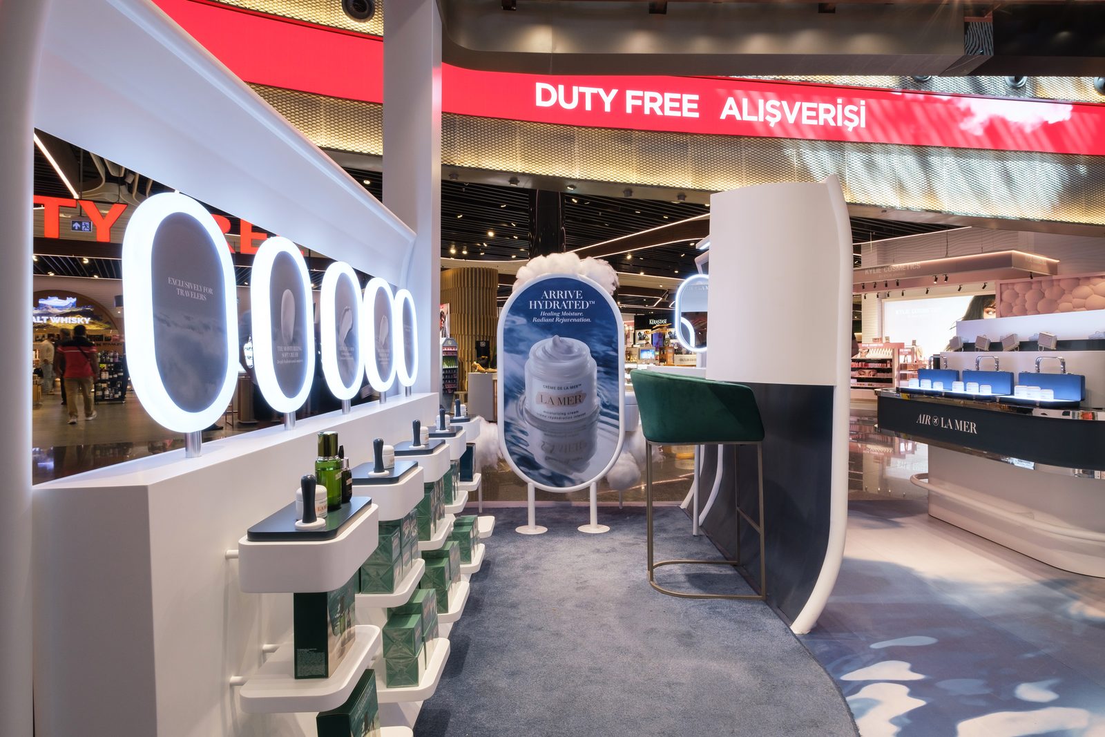 La Mer product wall with lit porthole frames and a lounge chair at Istanbul Airport duty free.