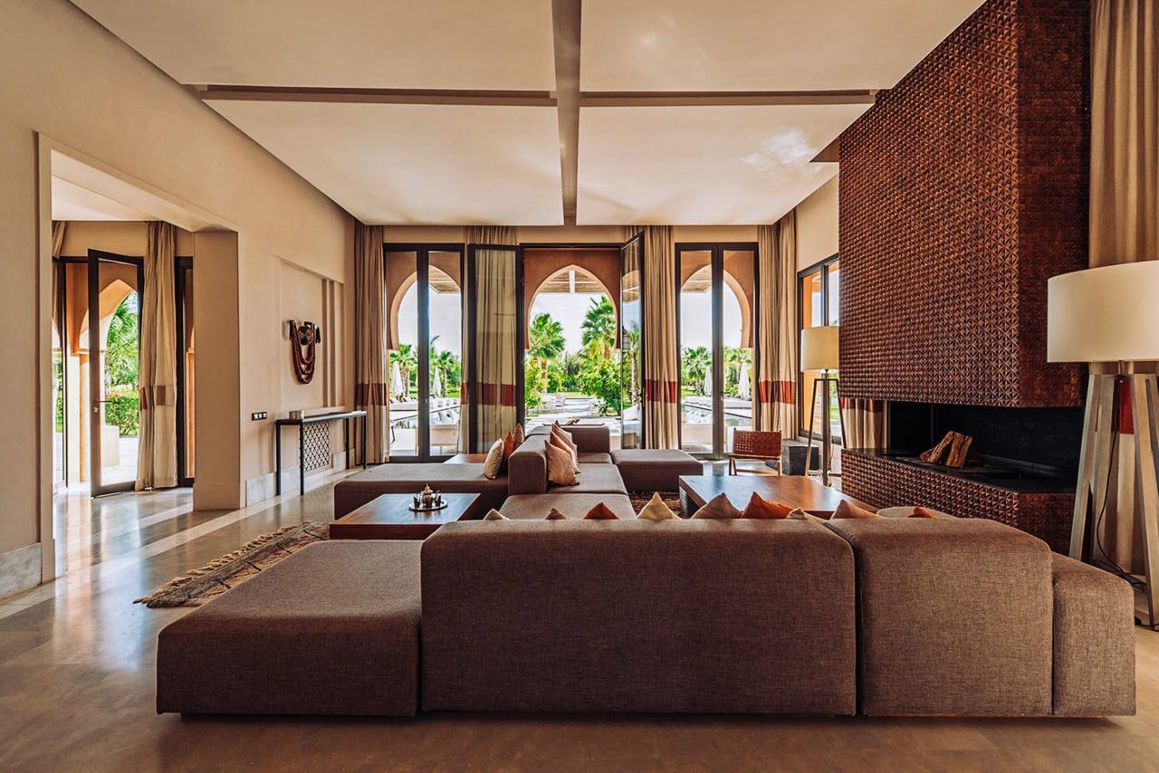 Moroccan villa living room with a sculpted brick fireplace and arched doors opening to the garden.