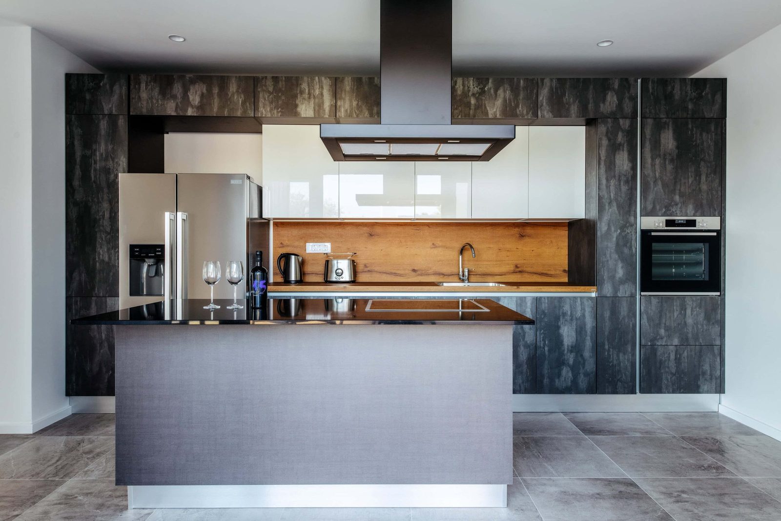 Stunning modern kitchen with sleek dark cabinetry, a spacious island, and built-in appliances. The design features minimalist style with warm wood accents and contemporary fixtures.