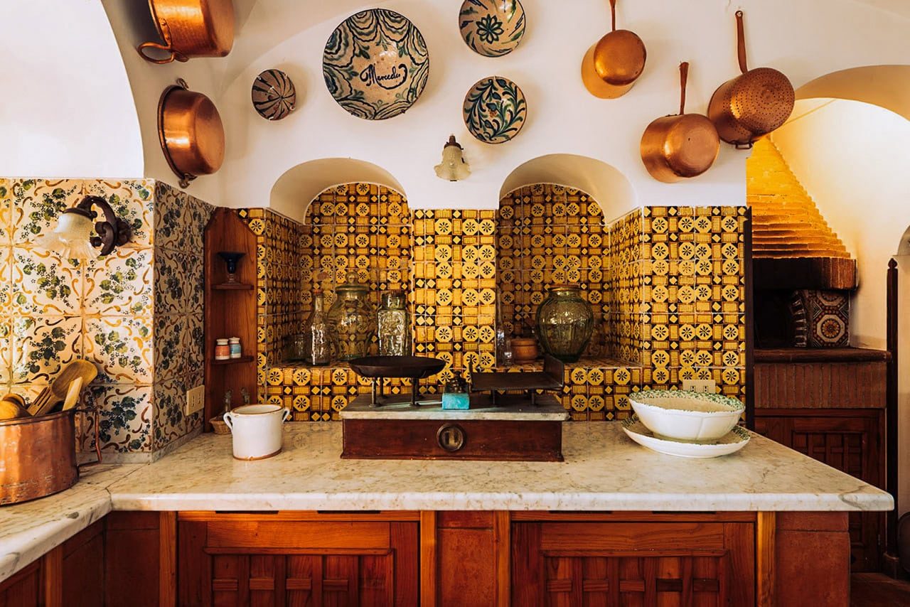 Copper cookware and decorative plates on a white arched kitchen wall, with a marble countertop and rustic wood accents, showcasing traditional Italian culinary style.
