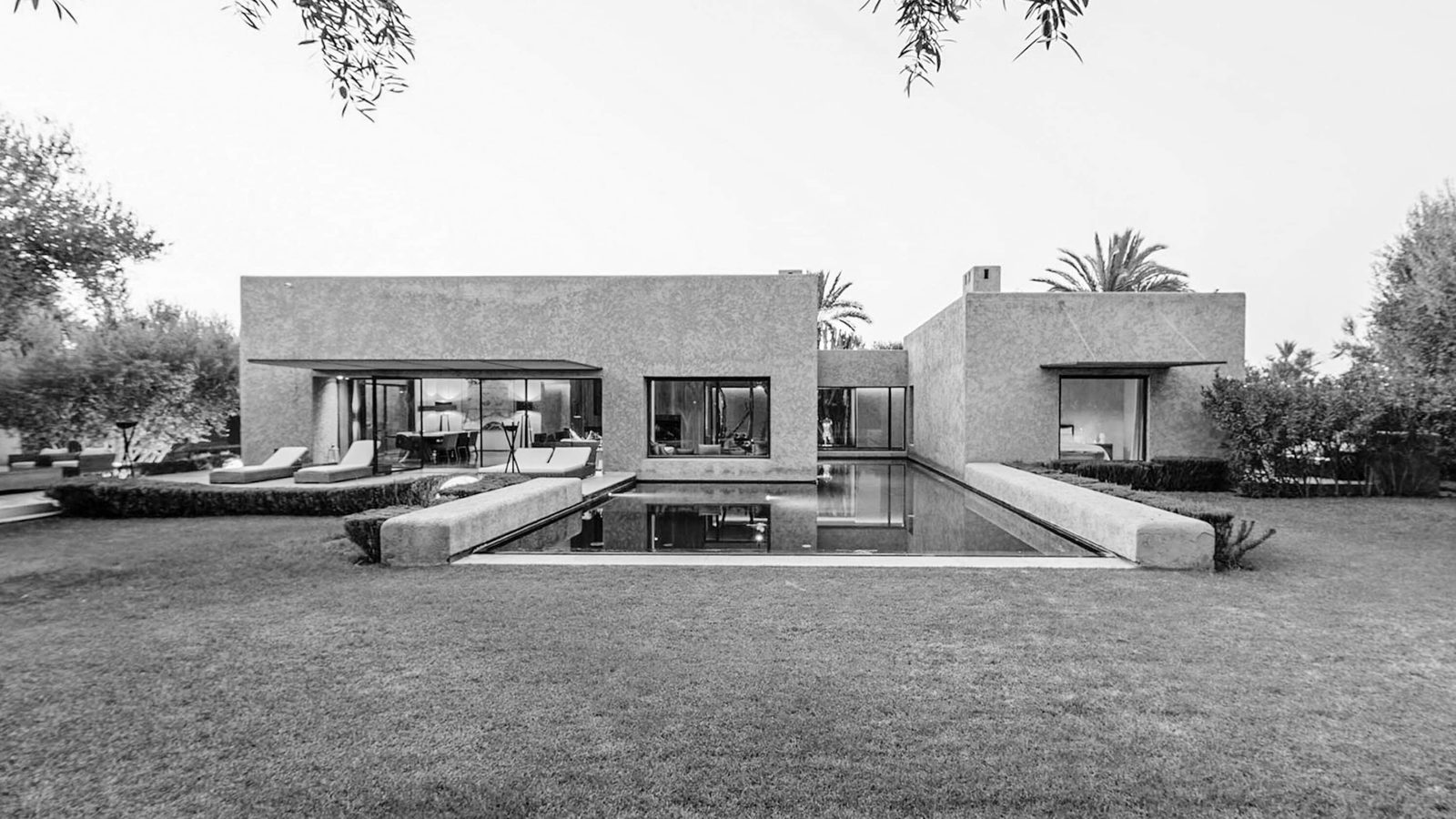 Vivienda minimalista moderna de diseño geométrico con piscina exterior en la parte trasera, rodeada de vegetación y arbolado, en blanco y negro.