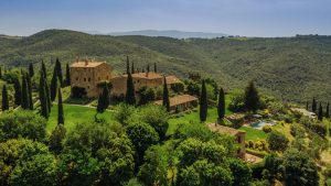 Luxurious Italian villa surrounded by lush greenery and rolling hills, captured in a high-quality aerial photograph showcasing stunning architecture and expansive gardens.