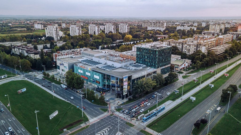 Aerial view of a modern shopping mall and surrounding cityscape in Madrid, Spain, showcasing architecture, greenery, and traffic.