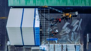 Factory construction site aerial view, industrial building being assembled with cranes and metal framework, urban manufacturing facility from above, professional architecture photography, TKM Photo Madrid Spain.