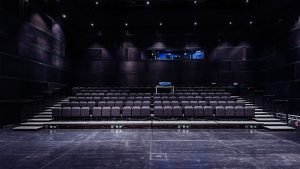 Modern theater interior with tiered seating, dark walls, and stage lighting, showcasing professional architectural photography by TKM Photo in Madrid, Spain.