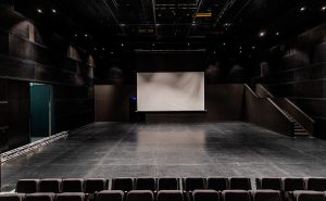 Empty black auditorium with a large white projection screen and black walls, interior of a modern cinema or conference hall, professional photography for architectural and industrial spaces, TKM Photo Madrid.