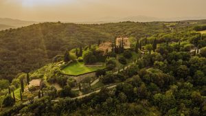 Lavish countryside estate surrounded by lush greenery, with cypress trees and stone buildings, captured during golden hour in Tuscany, Italy, showcasing architectural beauty and scenic landscape.