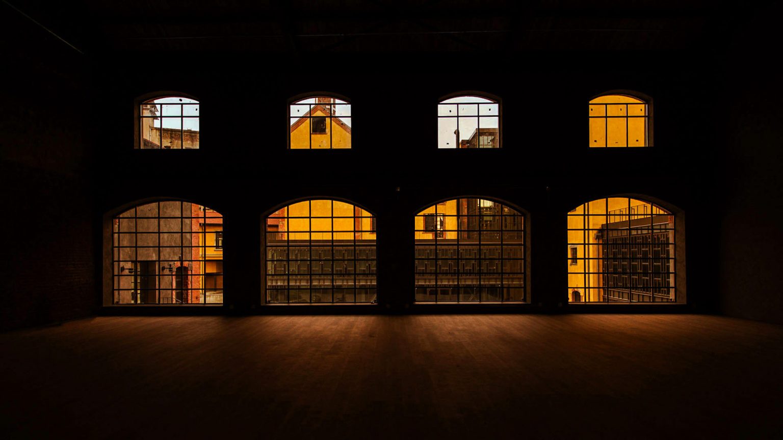 Madrid urban architecture captured at sunset, showcasing vibrant orange reflections on large industrial-style windows inside a spacious building.