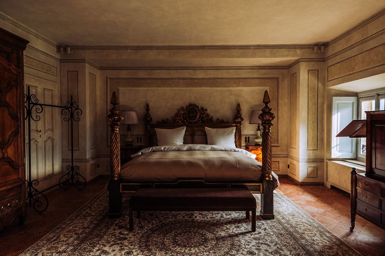 Elegante dormitorio con muebles de madera antiguos y decoración clásica, que cuenta con una cama grande con almohadas mullidas, lámparas de noche y una ventana que permite que la luz natural ilumine el interior vintage.