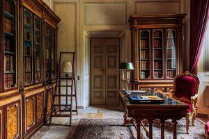 Luxurious historic library interior with antique wooden bookshelves, plush red velvet chair, elegant desk, and ornate details, showcasing classic architecture and refined decor.