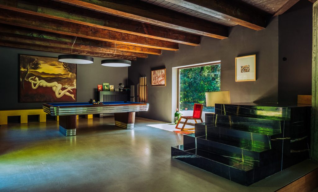 Modern interior with artistic decor and contemporary furnishings, featuring a sleek black staircase, colorful artwork on the walls, and abundant natural light from a large window.
