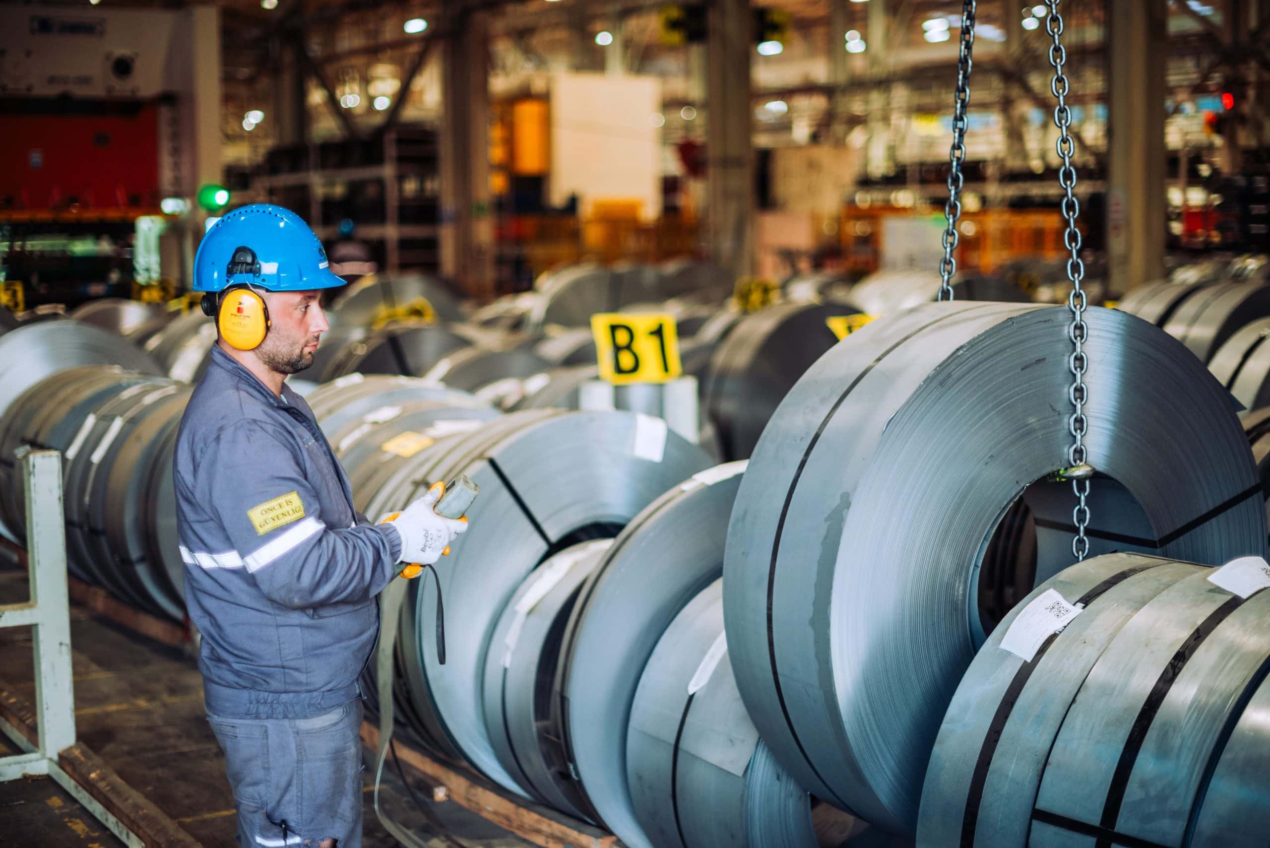 Bobinas de chapa metálica almacenadas en un almacén industrial con un trabajador inspeccionándolas, fotografiadas en un estilo profesional que enfatiza la manufactura y procesos industriales en Madrid, España.