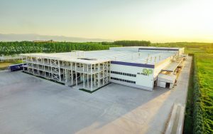 Aerial view of a modern industrial building with surrounding greenery and a bright, clear sky at sunset in Madrid, Spain.