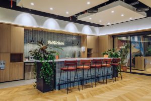 Modern hospitality interior with a sleek wooden bar counter, colorful bar stools, and vibrant greenery, showcasing professional commercial photography by TKM Photo in Madrid, Spain.