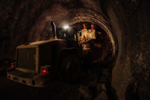 Excavator operating inside a dark tunnel under construction, with workers guiding the process.